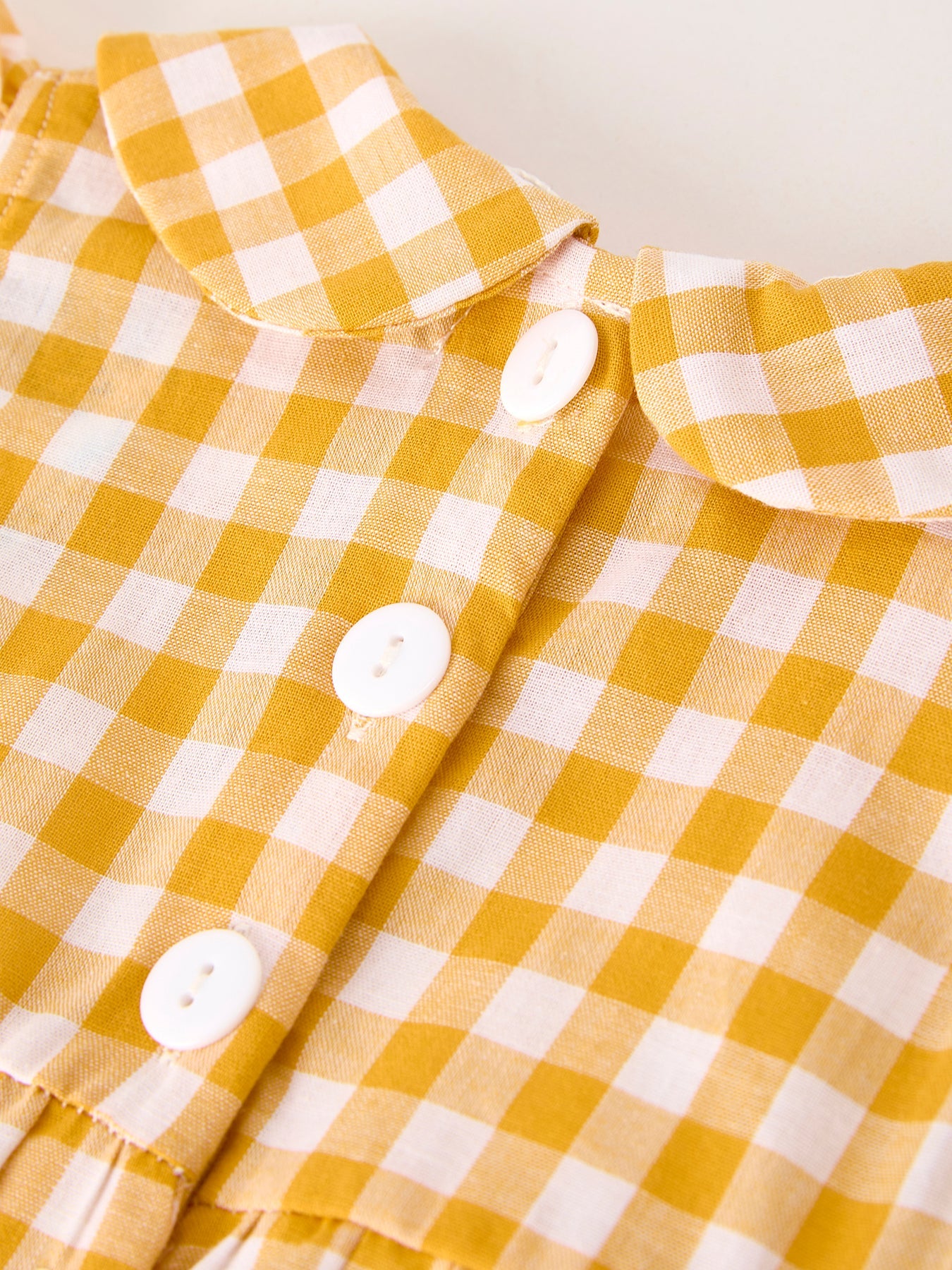 Baby girls yellow gingham bubble romper with pumpkin and turkey smocking, ruffle sleeves, Peter Pan collar, and bow accents.