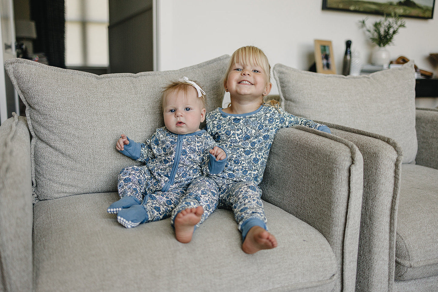 Two children in matching blue and white pajamas sitting on a beige couch.