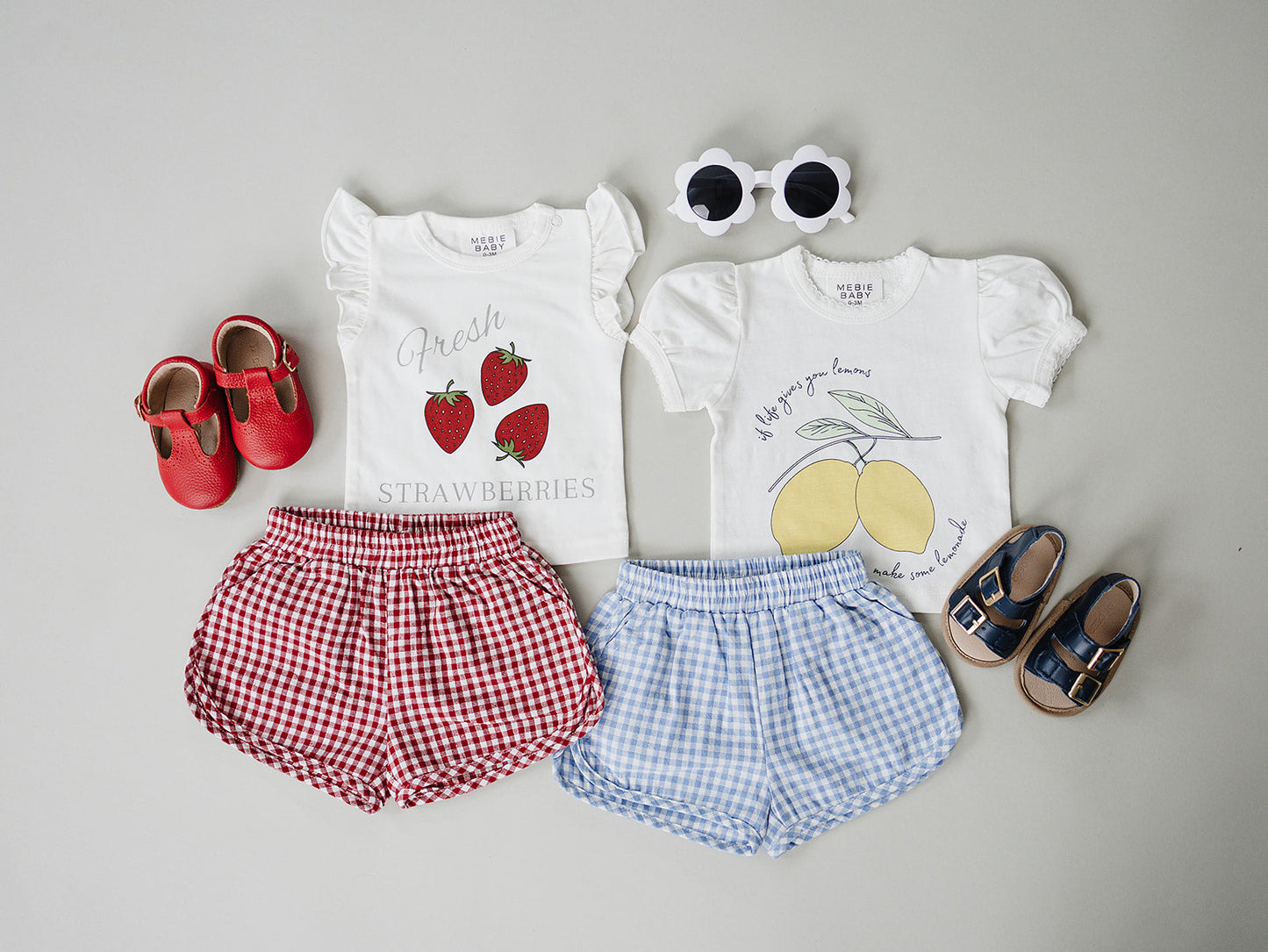 Children's clothing set with shirts, shorts, shoes, and sunglasses on a gray background
