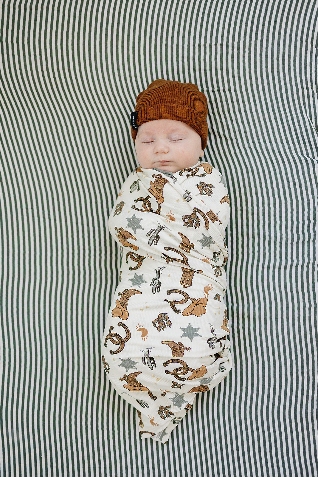 Newborn swaddled in western print baby blanket with cowboy hats and boots
