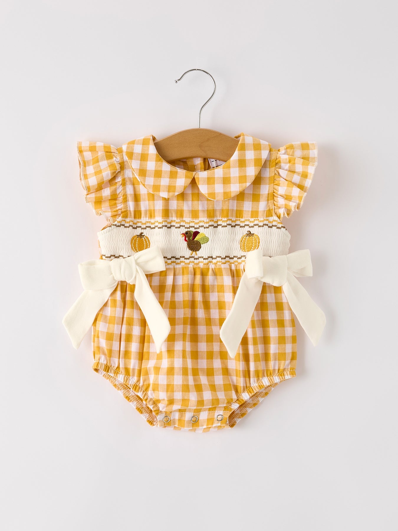 Baby girls yellow gingham bubble romper with pumpkin and turkey smocking, ruffle sleeves, Peter Pan collar, and bow accents.