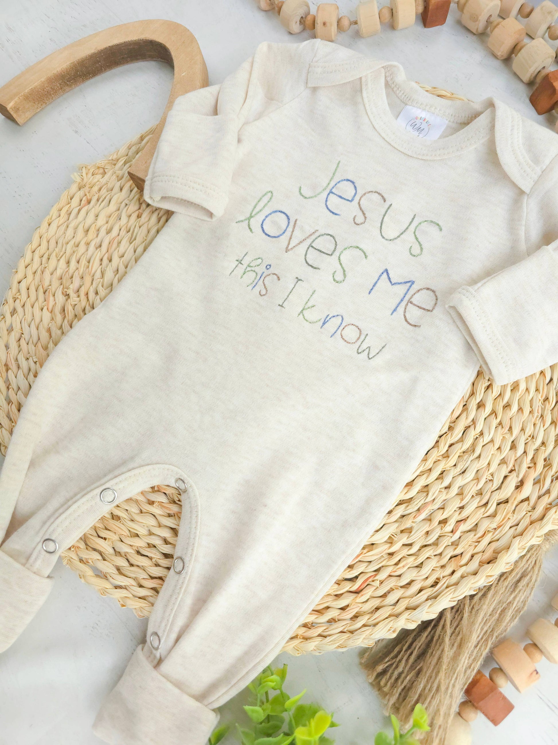 Baby onesie with 'Jesus loves me, this I know' text on a woven surface.