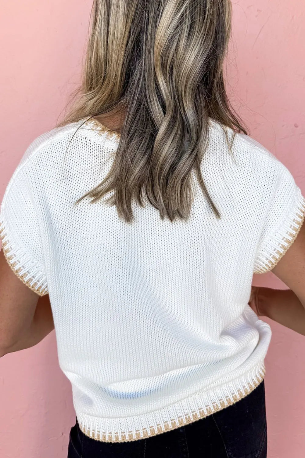 Person wearing a white knit top with a pink background