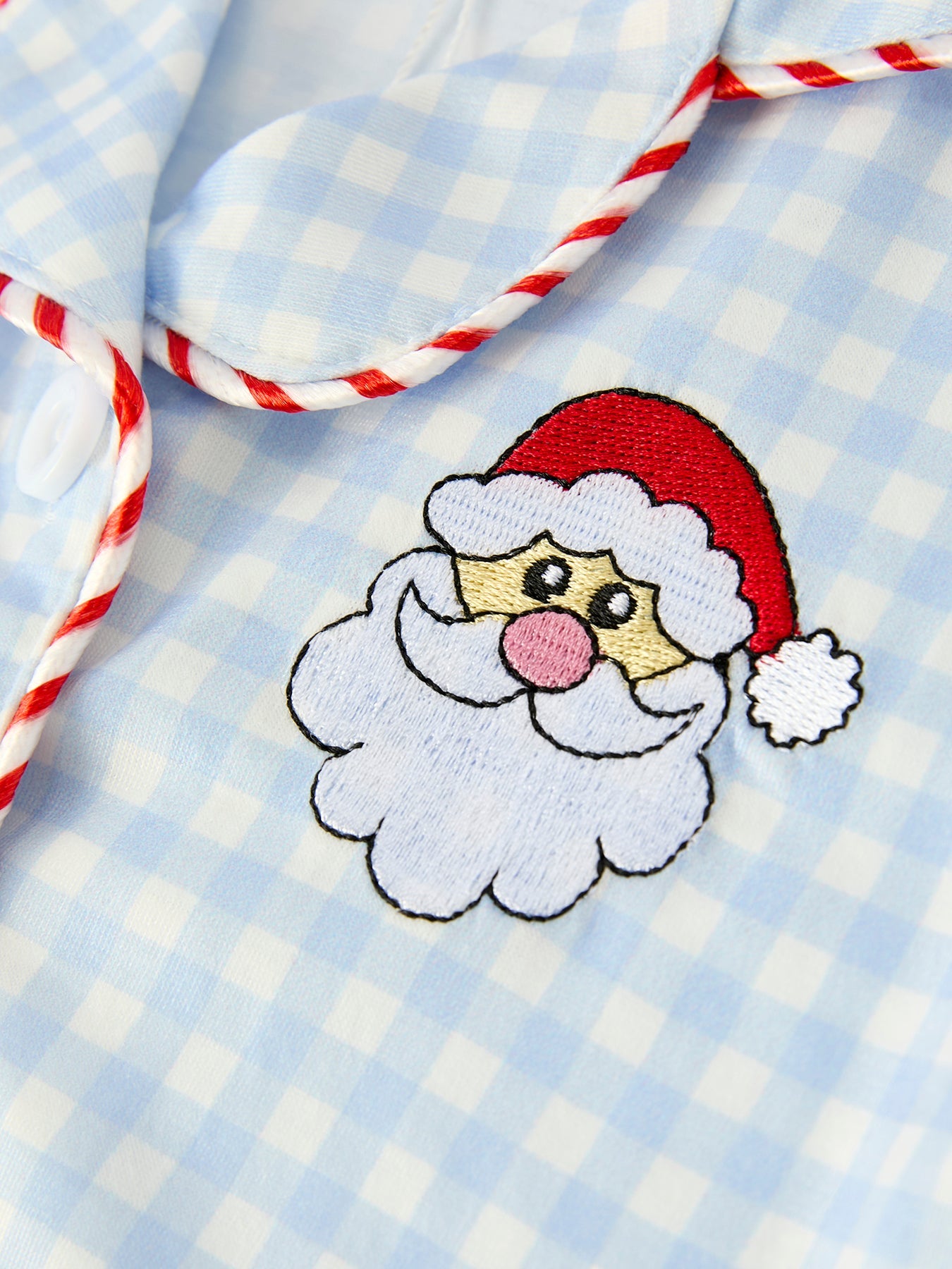 Close-up of Santa embroidery and red trim on blue gingham holiday pajamas.