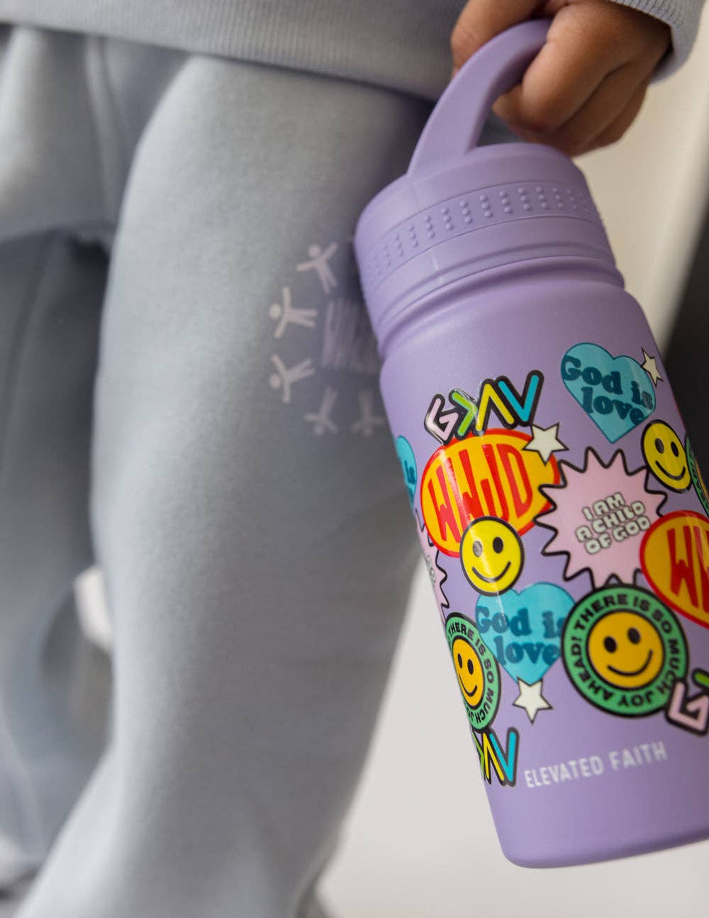 Purple water bottle with colorful designs held by a person wearing gray pants.