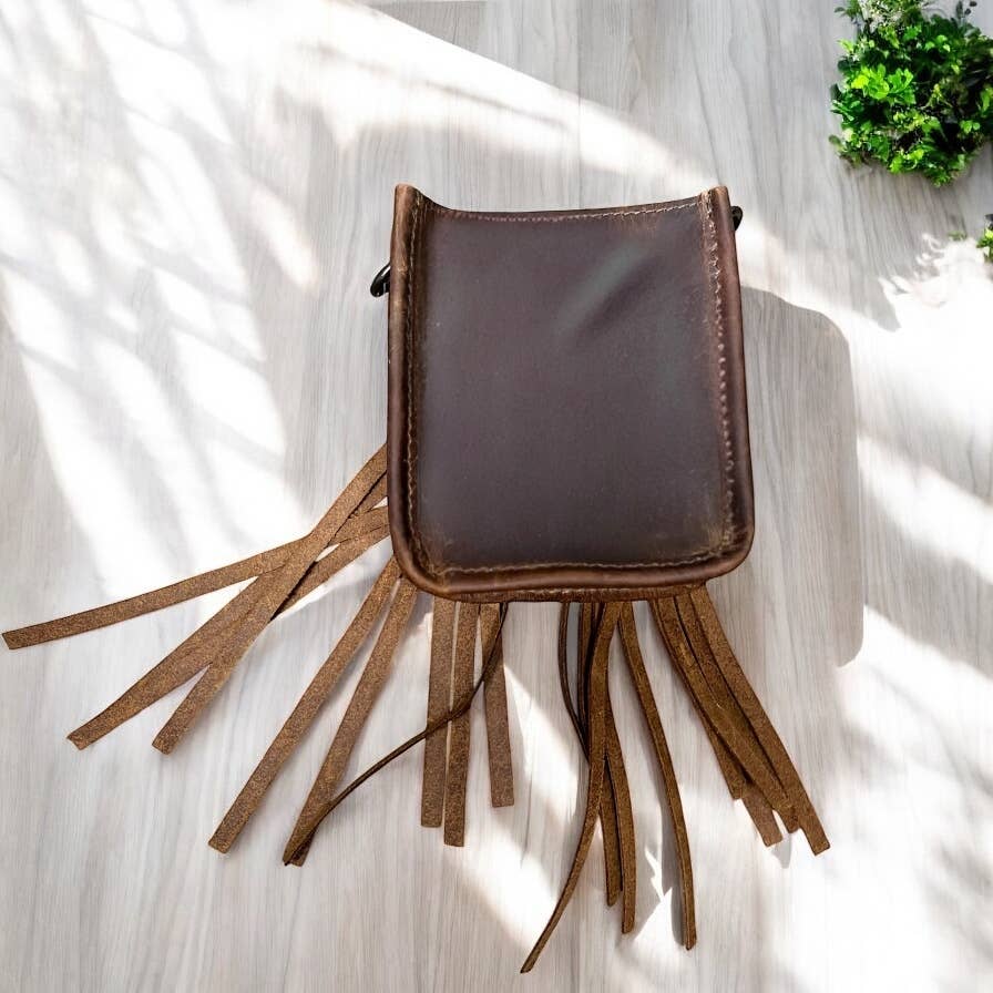 Brown leather crossbody bag with fringe on a light wooden surface
