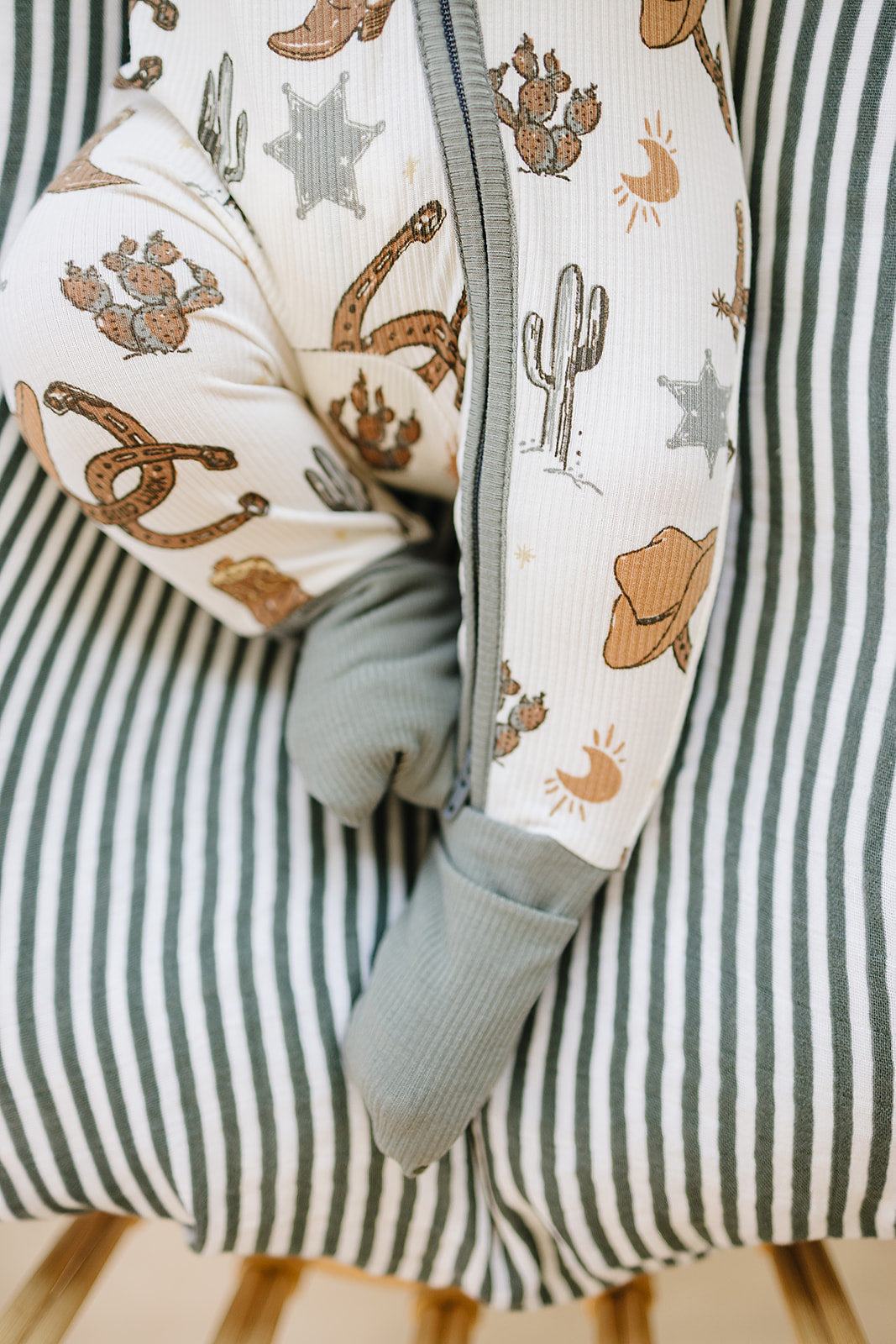 White baby zip-up pajama with green cuffs and western print