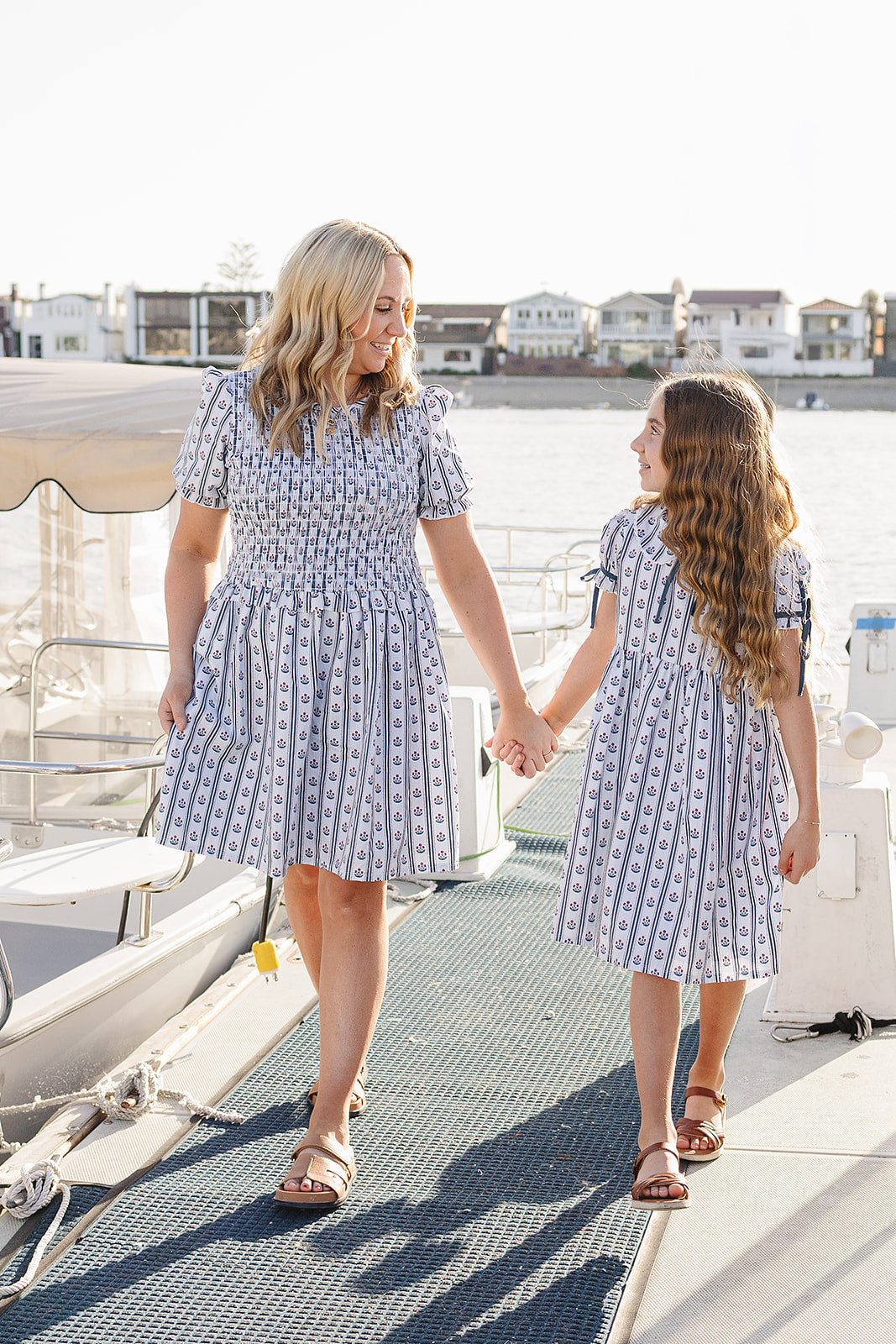 Young girl and her mom in matching blue patterned cotton dresses standing on a dock.