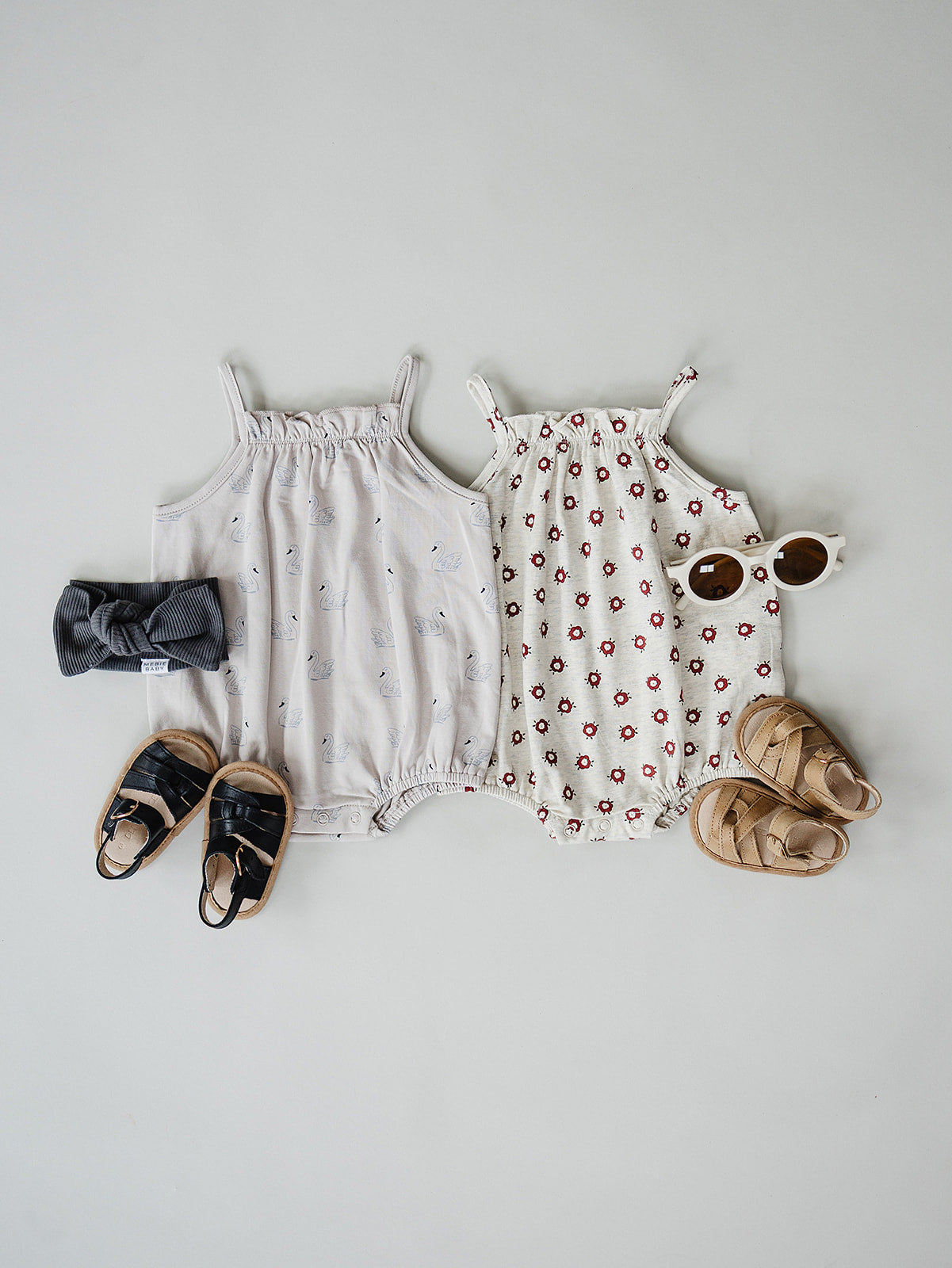 Two baby rompers with accessories on a light gray background