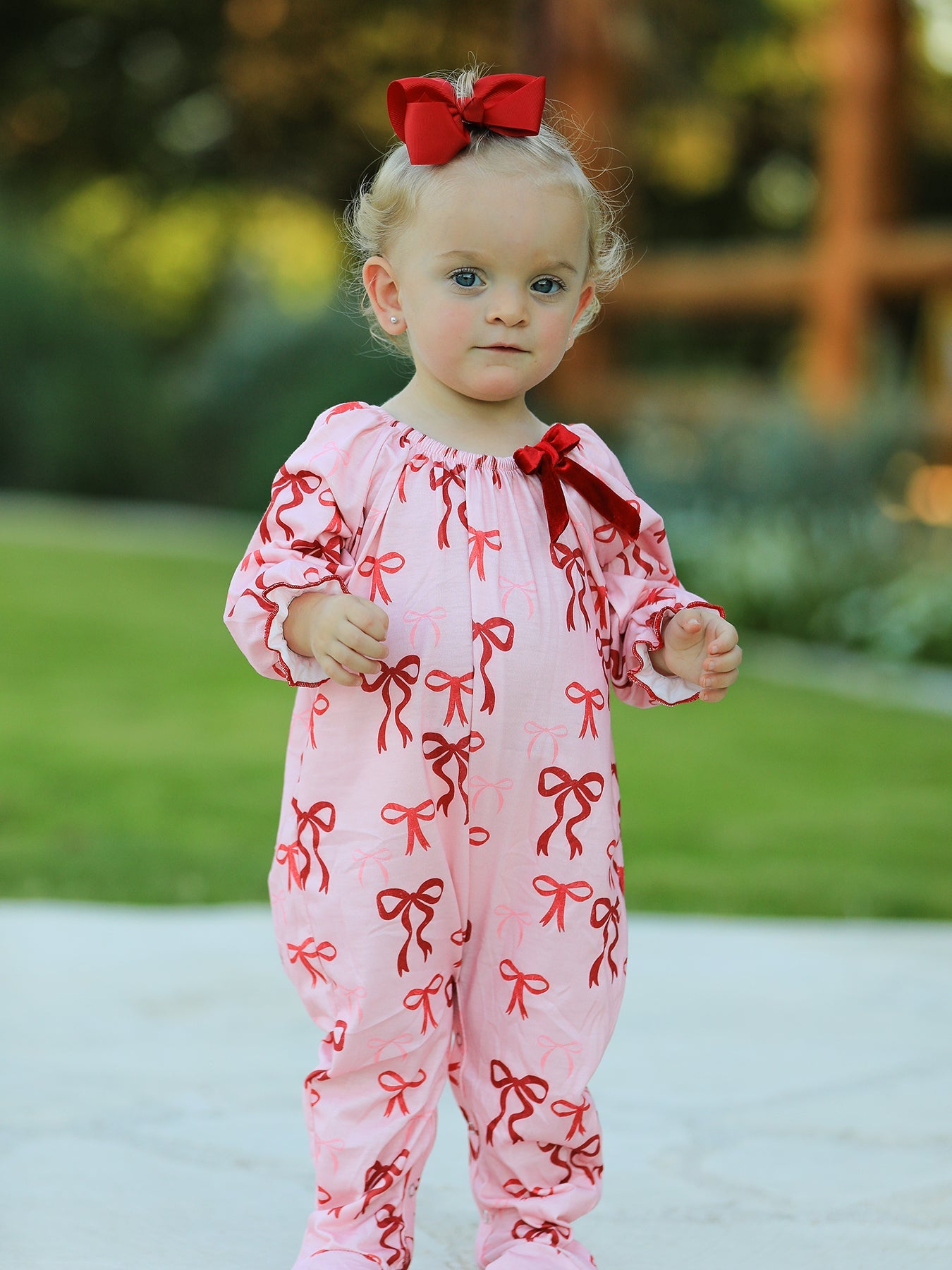 Baby girl wearing pink romper with red bow print and velvet bow