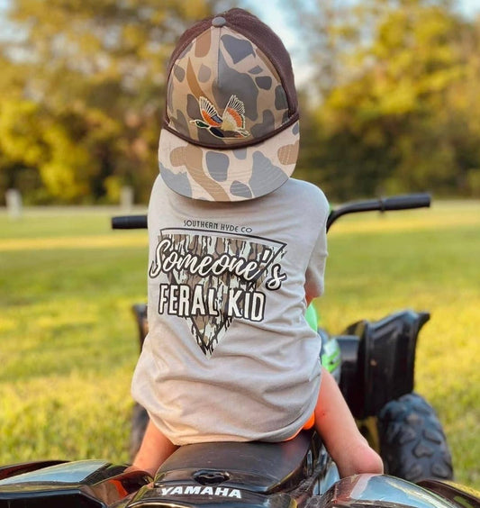 Toddler wearing Southern Hyde Co Someone’s Feral Kid camo graphic tee riding four wheeler outdoors