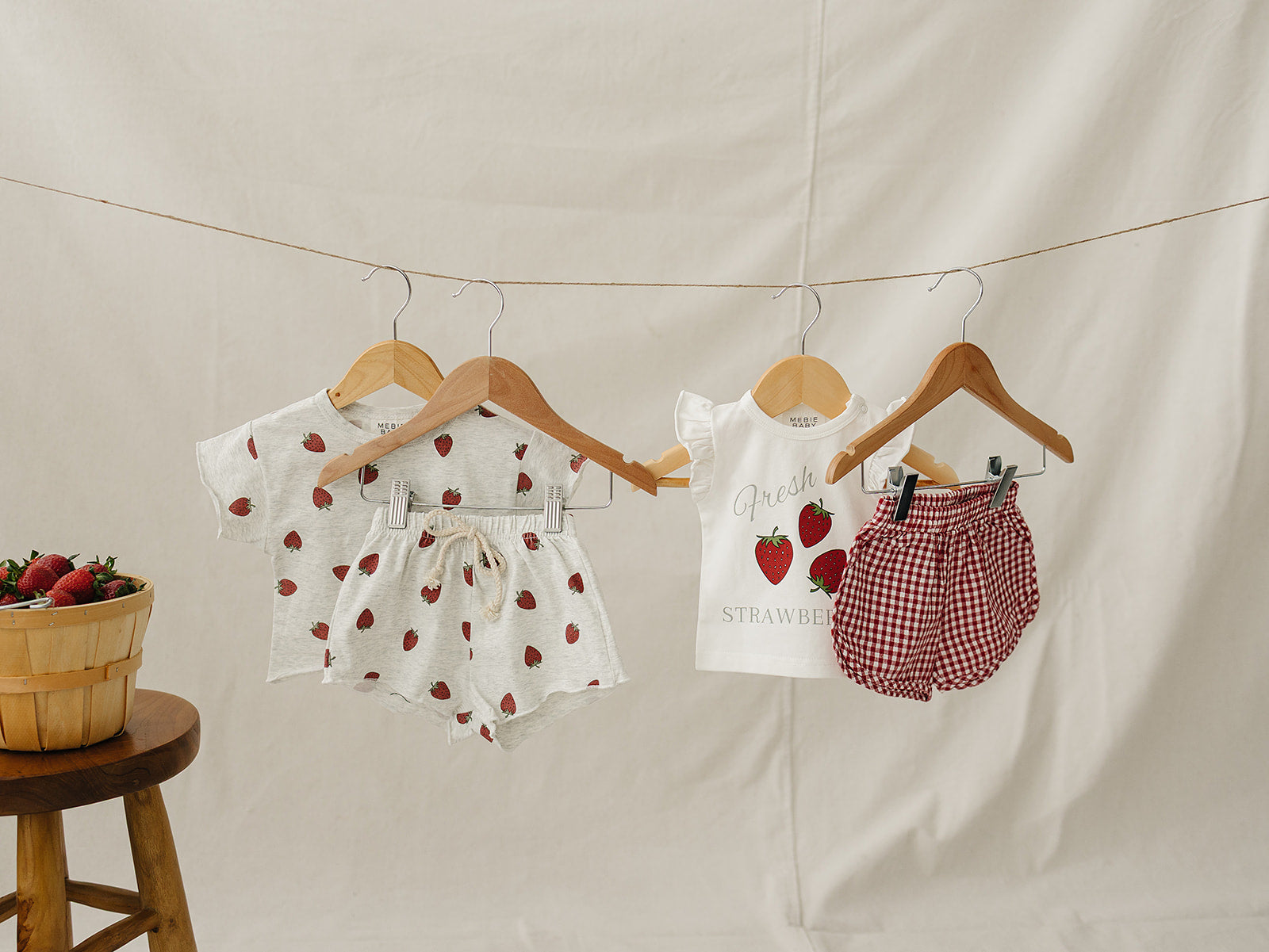 Children's clothing with strawberry pattern hanging on a line against a beige background.