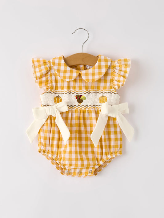 Baby girls yellow gingham bubble romper with pumpkin and turkey smocking, ruffle sleeves, Peter Pan collar, and bow accents.
