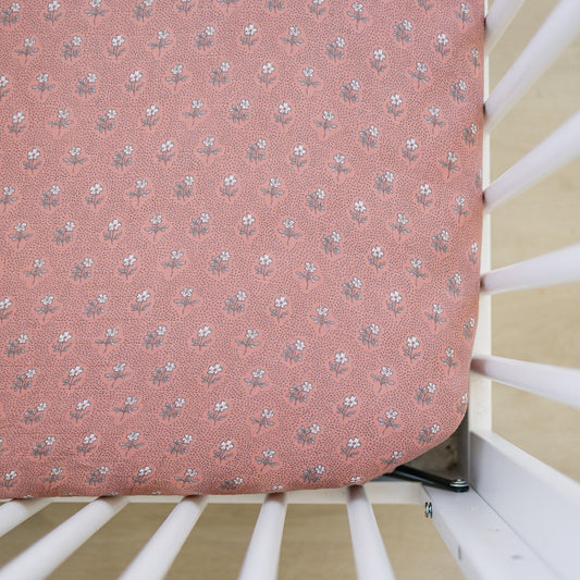 Pink floral-patterned ironing board cover on a white metal frame.