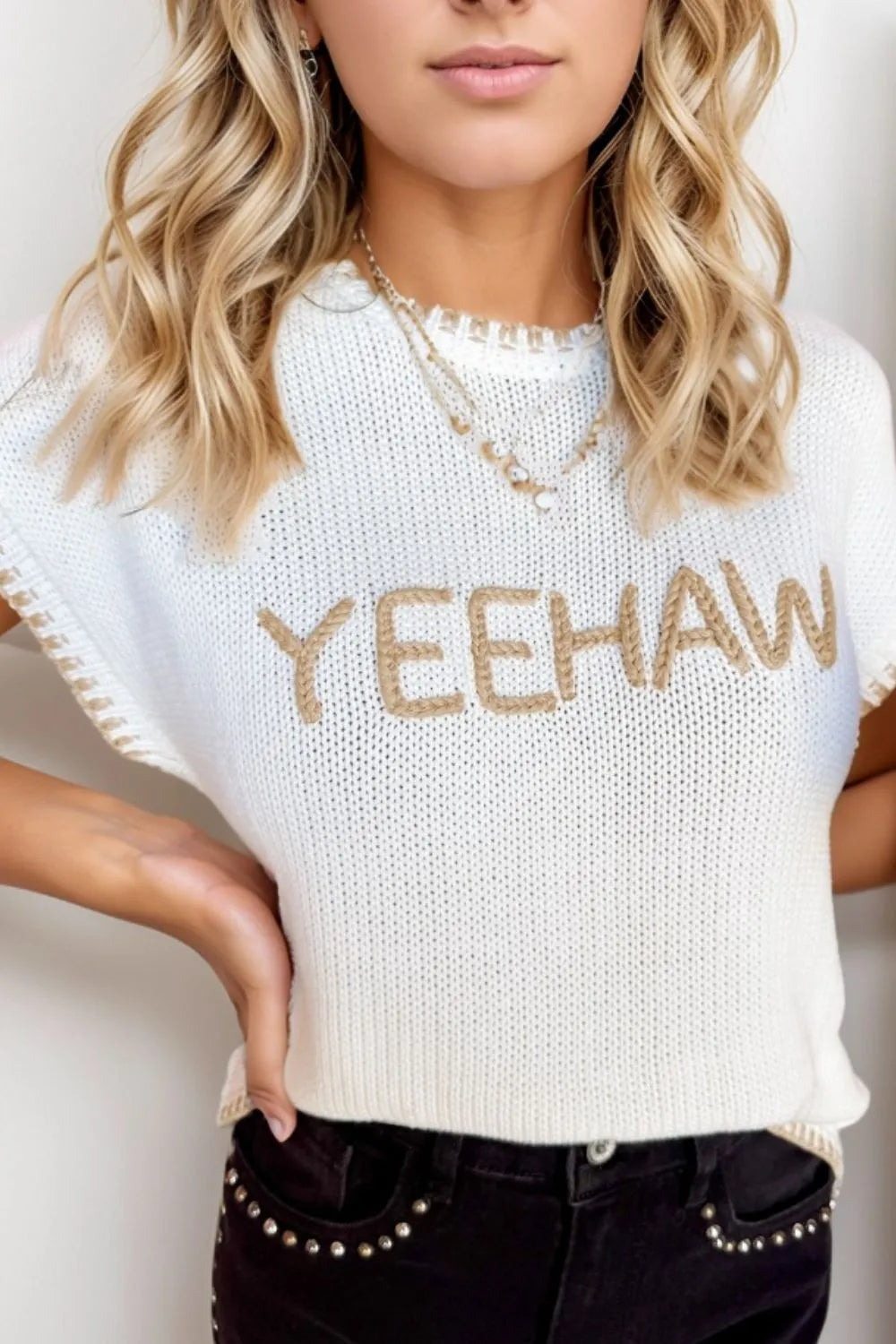 Woman wearing a white sweater with 'YEEHAW' text and black pants against a plain background
